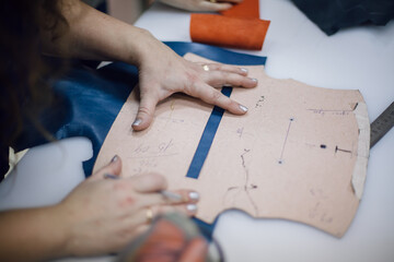 the girl puts a pattern for the bag on the skin. Women's hands on the pattern for the bag. She cuts...