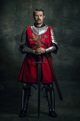Portrait of brutal seriuos man, medieval warrior or knight with dirty wounded face holding sword...
