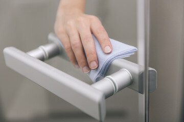 Cleaning glass door handles with an antiseptic wet wipe. Woman hand using towel for cleaning home room door link. Sanitize surfaces prevention in hospital and public spaces against corona virus