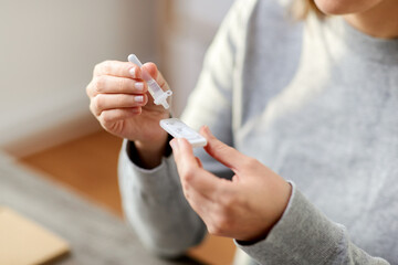 Obraz premium medicine, self testing and pandemic concept - close up of woman making coronavirus test and dropping reagent to cartridge at home
