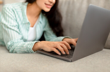 Cropped view of Indian woman using laptop while lying on couch at home