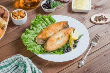 Fried fish fillet pieces with lemon and herbs on a white plate on a dark wooden background