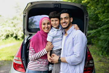 Fototapeta na wymiar Happy Muslim Family With Little Son Posing Near Car With Open Trunk