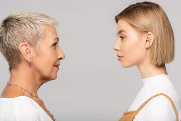 side view of young daughter and mature mother looking at each other isolated on grey