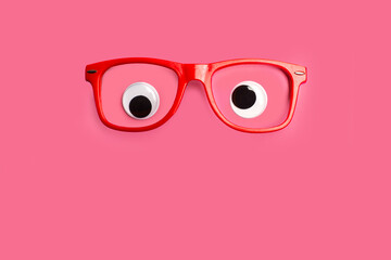 Ojos grandes y saltones de juguete con gafas rojas sobre un fondo rosa liso y aislado. Vista de...