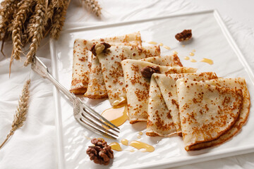 Homemade pancakes with walnuts and honey on a white fabric background. Pancake day.