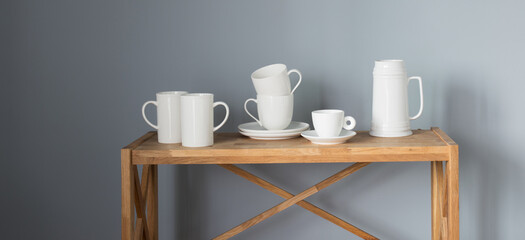 white cups and jug on wooden shelf on gray background