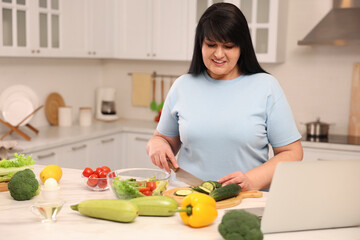 Beautiful overweight woman preparing healthy meal at table in kitchen