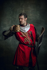Portrait of medieval warrior or knight with dirty wounded face holding shield and mug of beer...