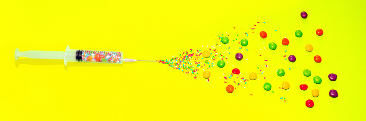 Syringe and needle, candy injection, spray colorful candies on a yellow background, children's injection, sweet and useful