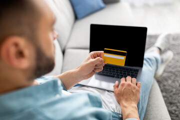 Contactless shopping, internet banking. Young man showing credit card, using laptop, buying goods online, mockup
