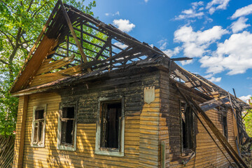 Fototapeta na wymiar Burnt wooden house on city street. Abandoned destroyed residential building. Consequences of fire, tragedy. Concept of fire careless handling
