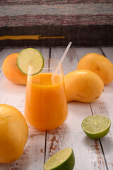 Orange drink closeup with lime slice on white vintage wooden desktop with mangos © ALEKSEI