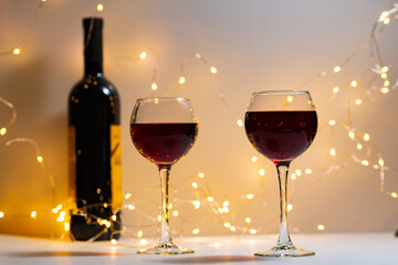 Horizontal photo of two side-by-side glasses of red wine and a bottle of expensive wine. Wine glasses with expensive red wine, bottle, light background, romance, Valentine's day, Christmas, new year.