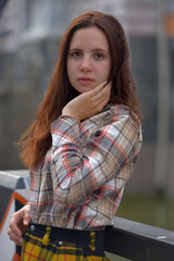 pretty brunette girl in a plaid blouse and skirt on a city street