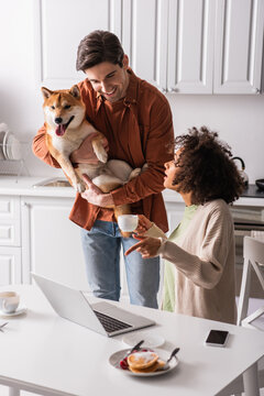 african american woman pointing at laptop near smiling boyfriend with shiba inu dog