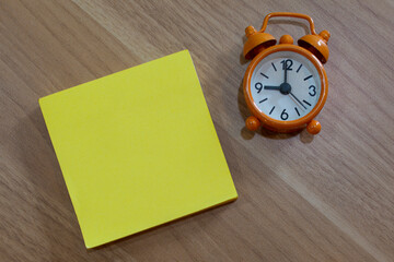 Yellow note with alarm clock on wooden desk. Flat lay