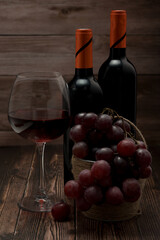 Bottled red, a glass of red wine and a small basket of grapes