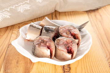 Several pieces of salted mackerel on a white ceramic plate on a wooden table, macro.