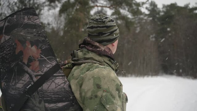 A hunter with a backpack and a gun behind his back looks around in the winter forest.