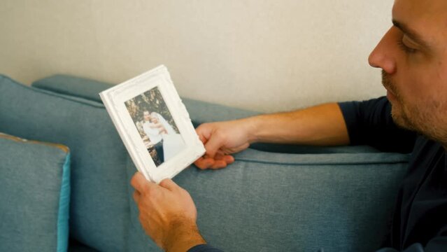 a man sits on the couch and looks pensively at his wedding photo and digests it face down