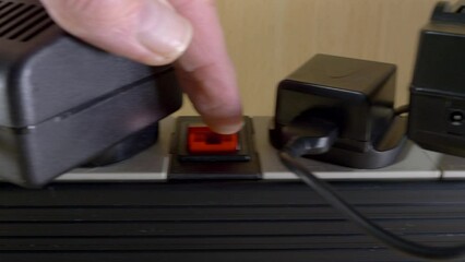 Closeup dolly shot of a man’s finger pressing the power switches for multiple devices, which are plugged into extenstion board sockets for a UK 240 volt electricity supply.