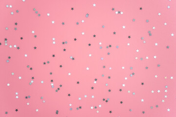 Silver stars glittering confetti on pink background. Trendy festive holiday backdrop. Many star-shaped particles for a postcard, invintation or web banner