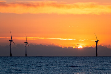 Solar and wind power. Wind turbines on the sea horizon at sunrise.