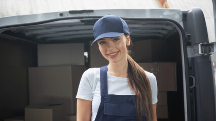 Happy delivery woman smiling at camera near car with packages outdoors