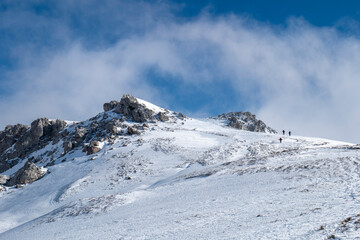 Mountaineers walking, hiking on a winter sunny day to reach the mountain peak. Wind and clouds are...