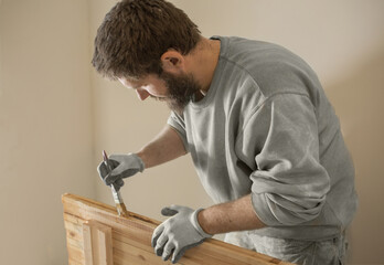 a man with a beard varnishes a wooden board with a brush.