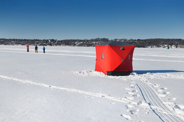 Family hiking on frozen lake and red ice fishing tent on Kempenfelt Bay of Lake Simcoe in winter...