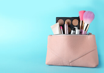 Cosmetic bag with makeup products and accessories on light blue background. Space for text