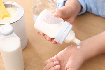 Woman checking temperature of infant formula at table, closeup. Baby milk