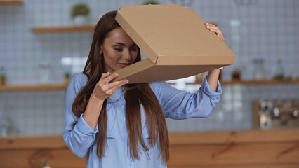 Brunette woman smelling open pizza box at home