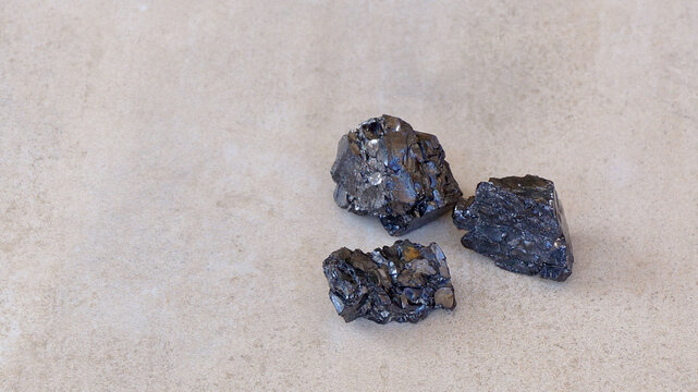 Three Black Shungite Mineral Stones On Light Brown Background Copy Paste