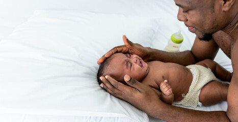 Blurred soft images of African baby newborn Lying on white bed and crying with father comforting, to relationship of African family and newborn concept.