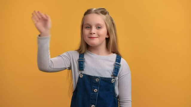 Portrait friendly smiling female kid waving hand with positive emotion posing isolated on orange 