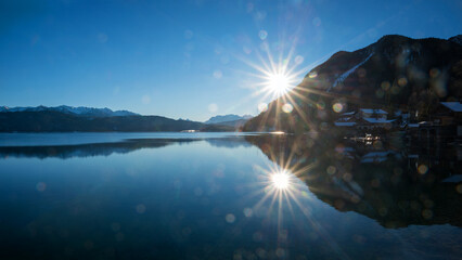 sunset at lake shore Walchensee, bright sun with rays, flares and water reflection