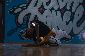 Fototapeta na wymiar African American hip hop dancer (breakdancer) performing over graffiti background in dark silhouette exposure.
