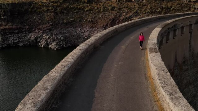 Aerial shot of an Asian woman hiking across the historic 100 year old Salmon Falls Dam in Southern Idaho