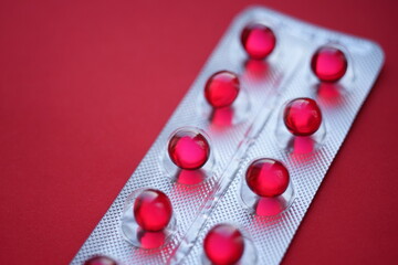 Red round pills vitamins capsules in a blister pack on a red table