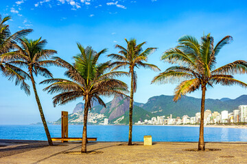 Fototapeta na wymiar View of Ipanema beach in Rio de Janeiro on a summer morning with palm trees, rocks, hills, ocean and buildings