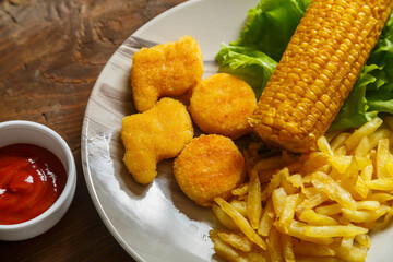 Nuggets, french fries and corn on the cob on lettuce leaves on a plate on a napkin.
