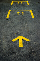 Yellow arrow and footsteps street guide sign on black asphalt. Guidance and regulation of social distancing during a global pandemic.
