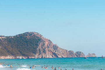 A mountain near a beach with lots of people swimming. Turkey, Alanya