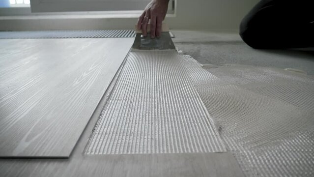 Worker Uses Scraper To Smear Glue On Floor Before Gluing Vinyl Or Laminate Tiles