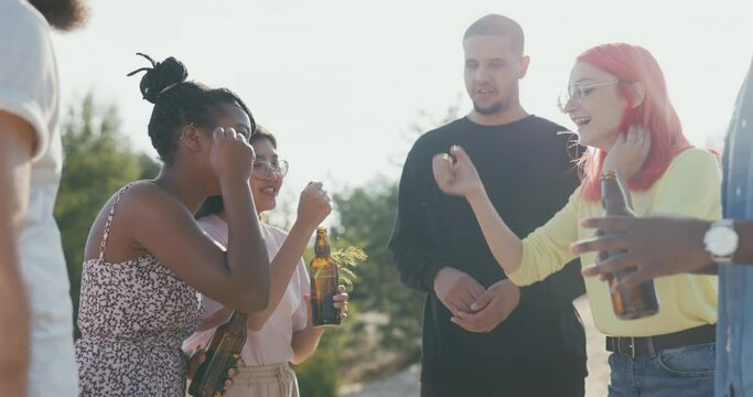 A group of friends of different nationalities spend their time at lake drinking beer from glass bottles, playing rock-paper-scissors, drawing lots to see who will be the driver, betting on something