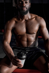 Fototapeta na wymiar Close-up Portrait Of Relaxed African American Man Sitting In Gym With Water Bottle, Exhausted And Tired Black Man After Training Workout. Muscular Fit Sportsman Taking A Break. Model With Perfect Body