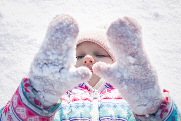 winter portrait of a little girl who covers her face with mittens in the snow